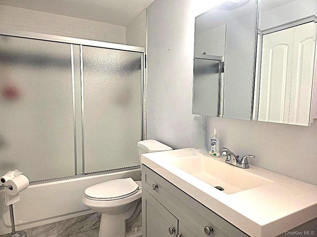 Bathroom with a white vanity, mirrored cabinet, toilet, and frosted-glass shower.