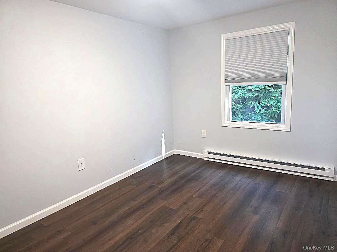 Empty room with dark wood-look flooring, gray walls, and a window with a partially lowered blind.