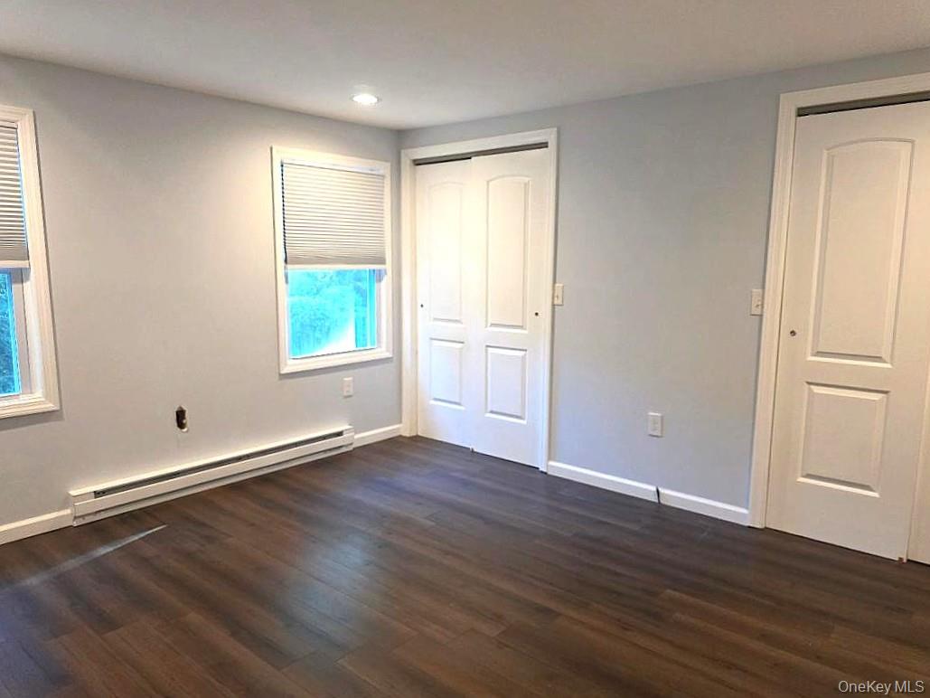 Unfurnished room with dark wood floors, gray walls, two windows, and white closet doors.