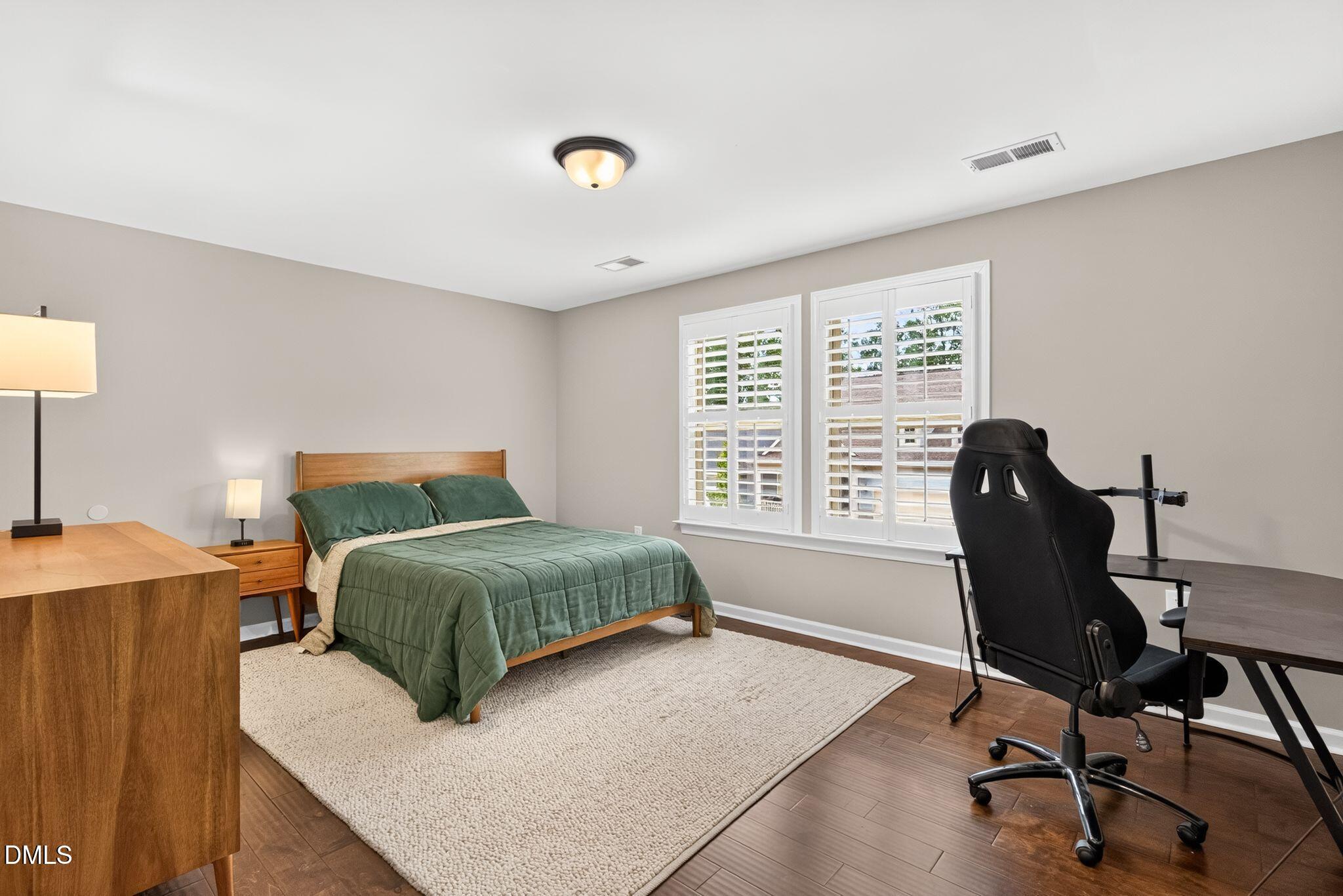 Bedroom with a green-quilted bed, shuttered windows, and a desk with a black office chair.