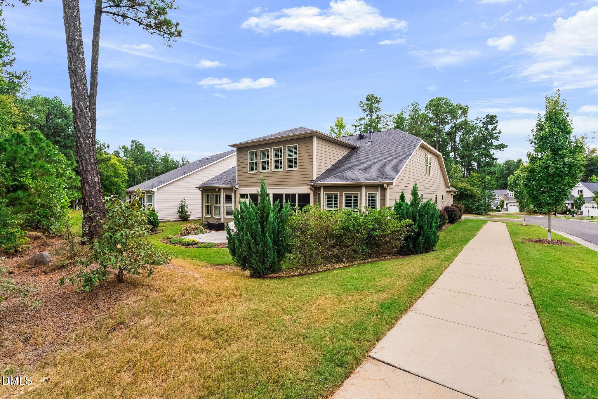 Rear of a tan two-story house with a screened patio, landscaped shrubs, and a sidewalk.