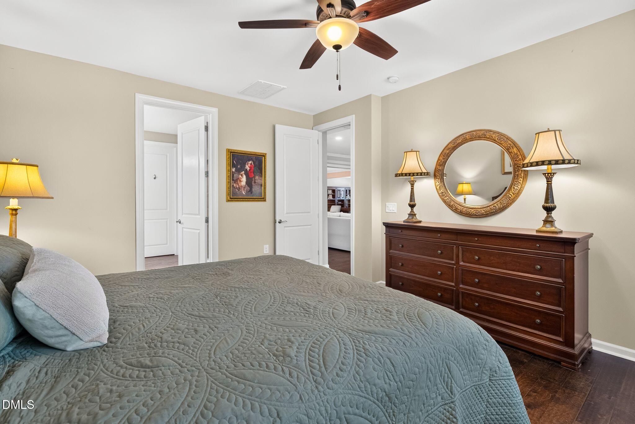 Furnished bedroom with a gray quilted bed and dark wood dresser beneath an ornate round mirror.