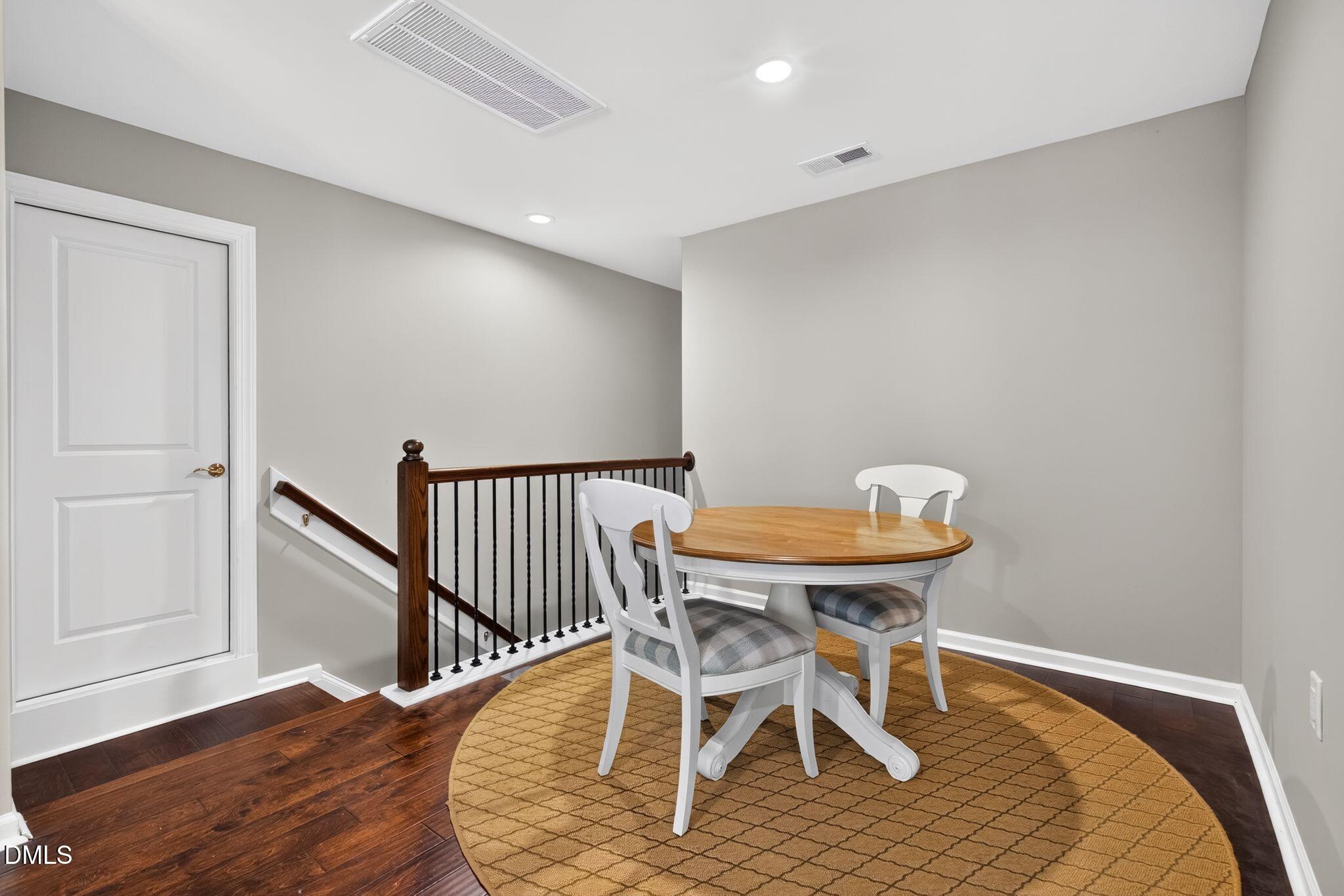 Dining area with a round wooden table and white chairs beside a staircase.