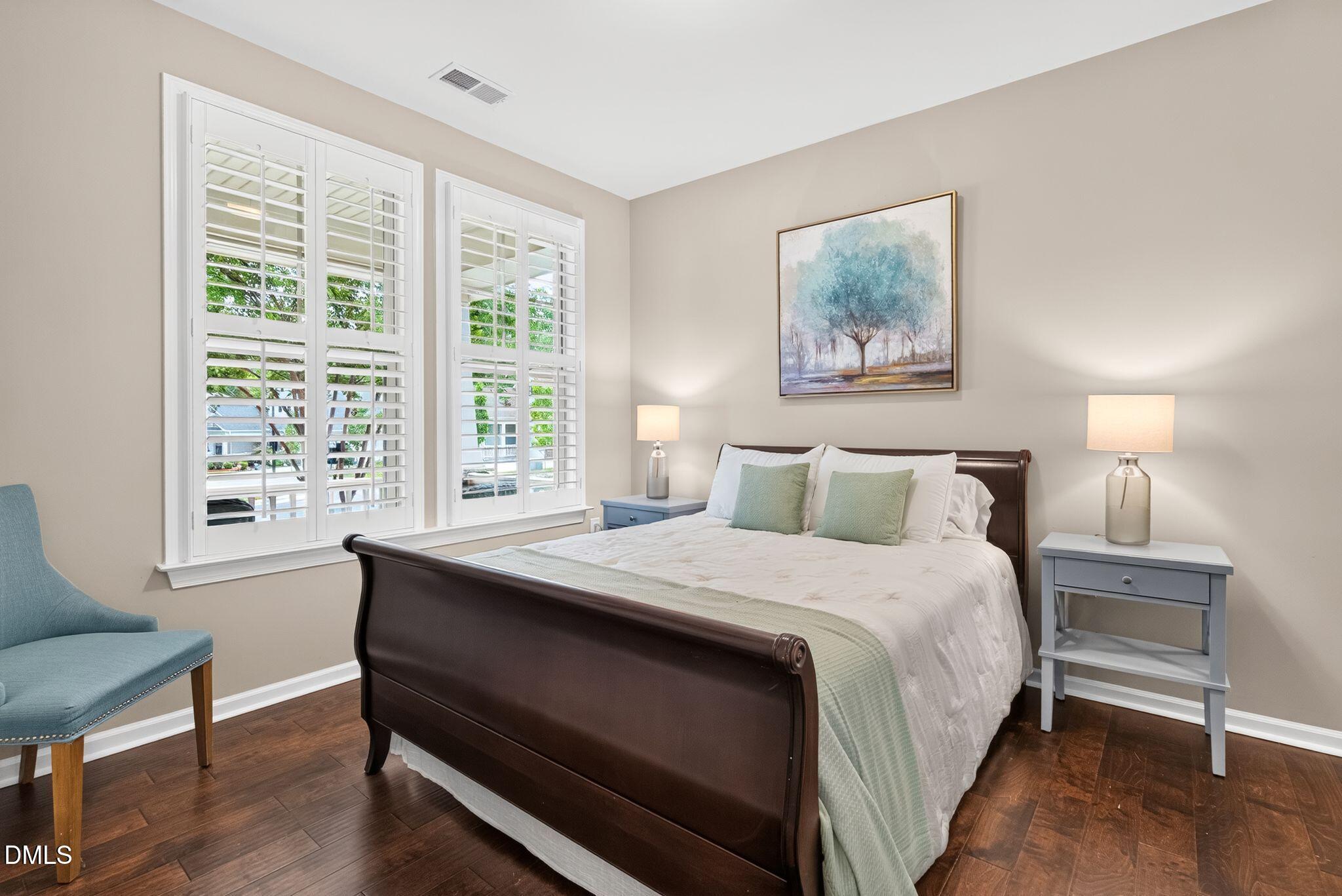 Staged bedroom with a dark wood sleigh bed, plantation-shuttered windows, and hardwood floors.
