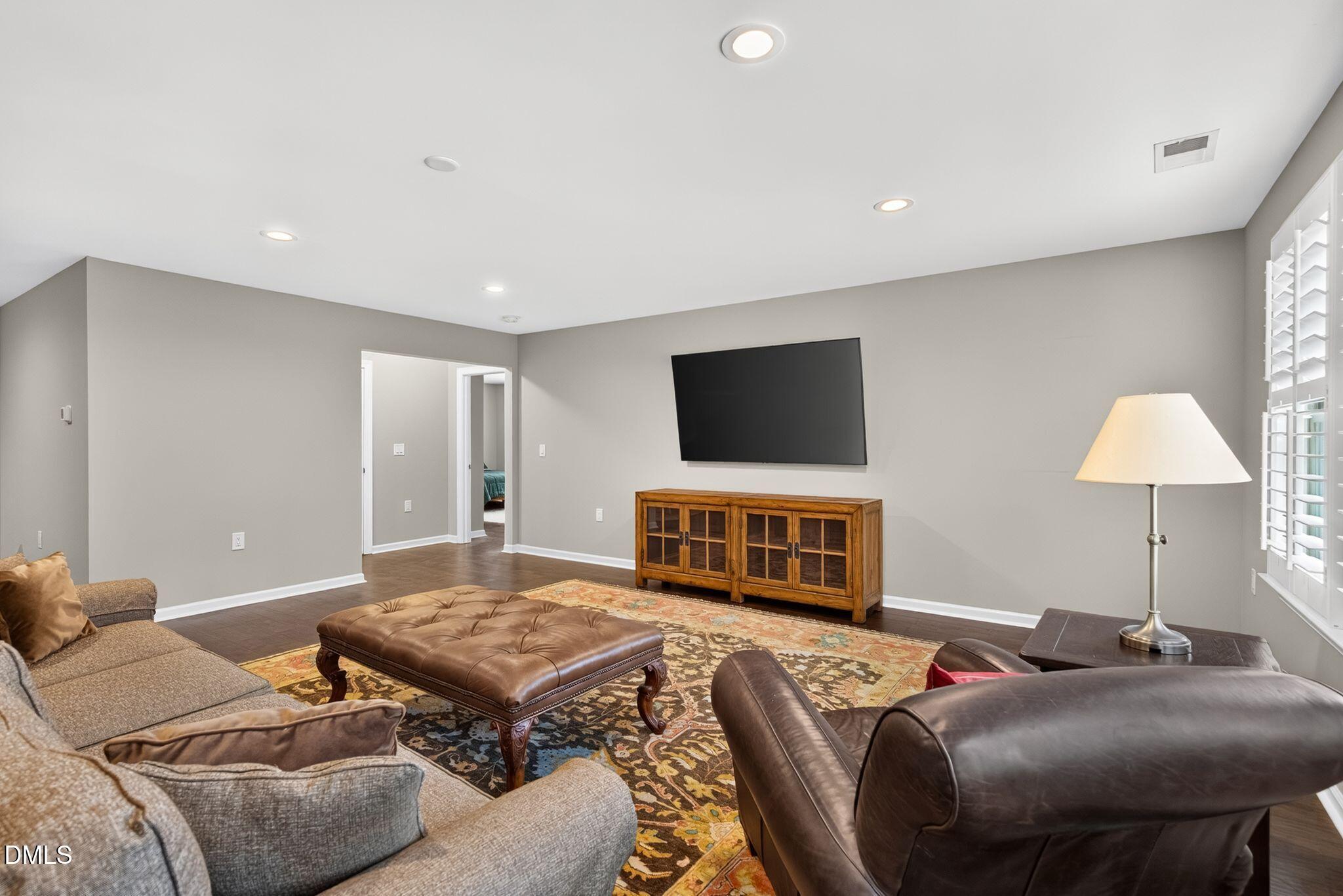 Furnished living room with a wall-mounted television, patterned rug, and plantation shutters.