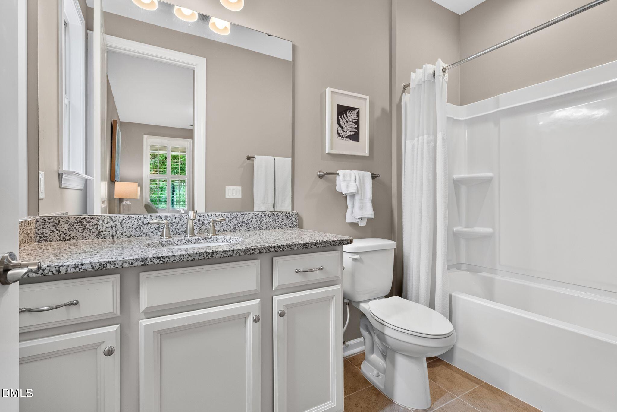 Bathroom with granite vanity, large mirror, and white tub-shower.