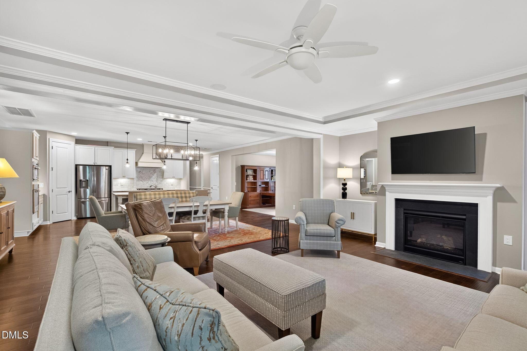 Open-plan living room with a white fireplace, large sectional, and adjoining kitchen and dining area.