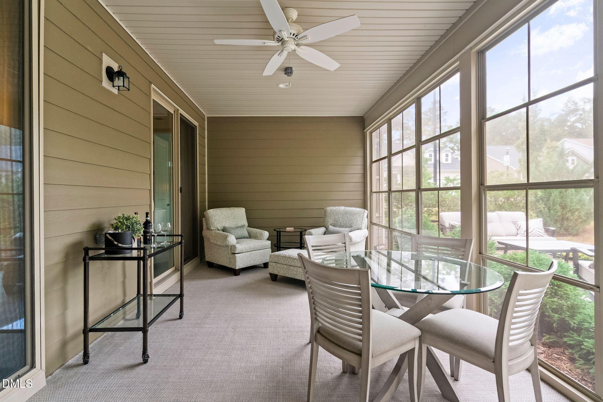 Furnished sunroom with a glass dining table, armchairs, and large windows overlooking greenery.