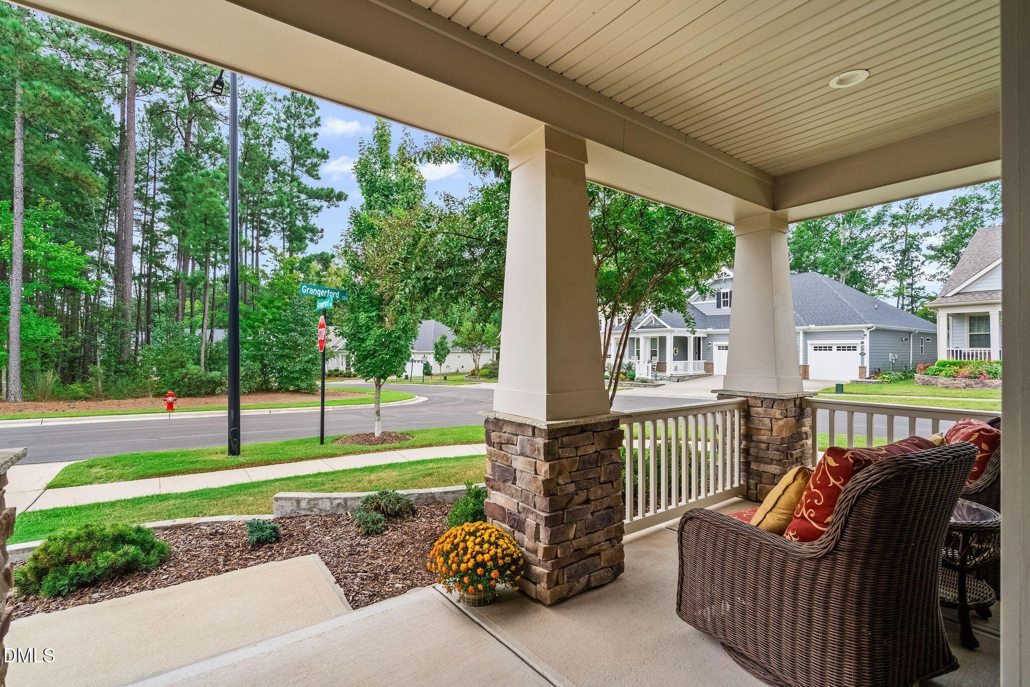 Covered front porch with stone columns and wicker seating overlooking a landscaped yard.