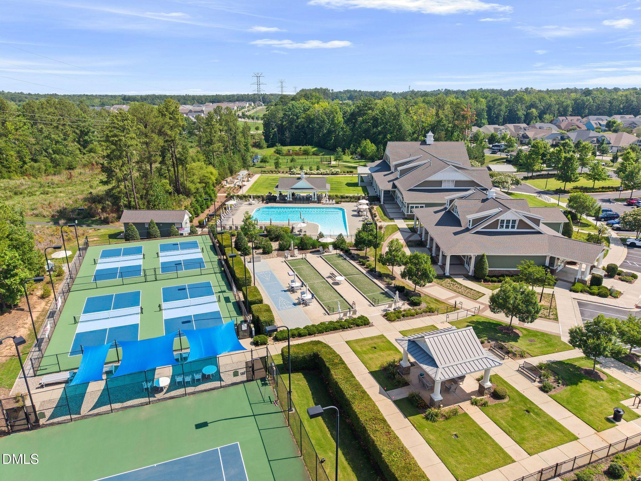 Community clubhouse and pool beside fenced courts and landscaped paths, viewed from above.