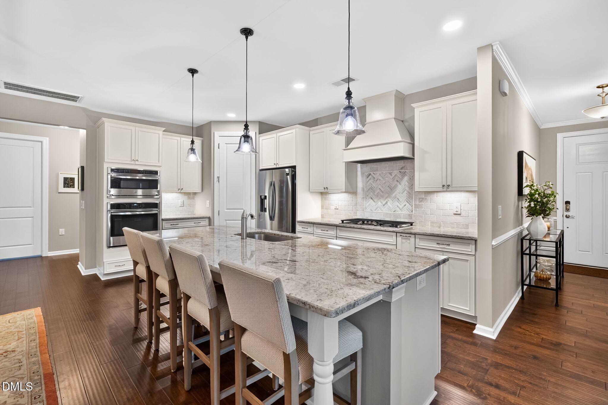 Kitchen with a large granite island, bar stools, white cabinets, and stainless steel appliances.