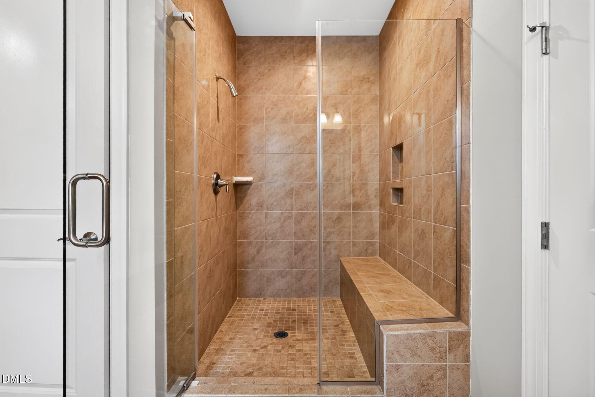 Walk-in shower with warm brown tile, a glass enclosure, built-in bench, and recessed niches.