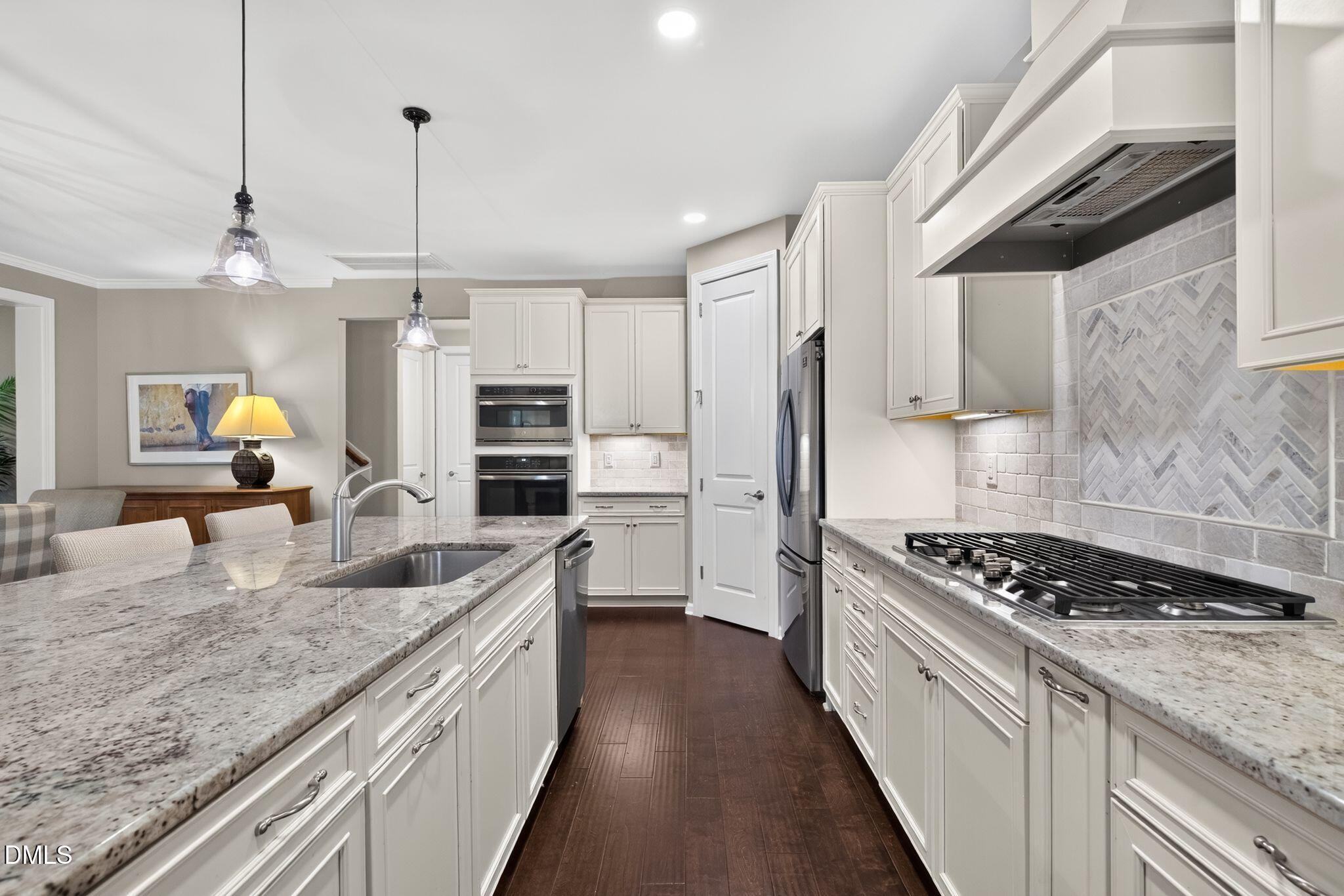 Kitchen with white cabinetry, granite island, stainless appliances, gas cooktop, and gray herringbone backsplash.