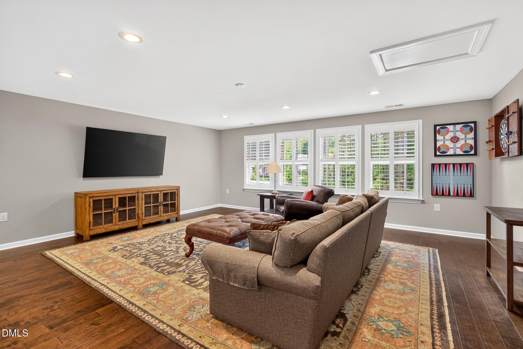 Furnished living room with a wall-mounted television, brown sectional, patterned rug, and shuttered windows.