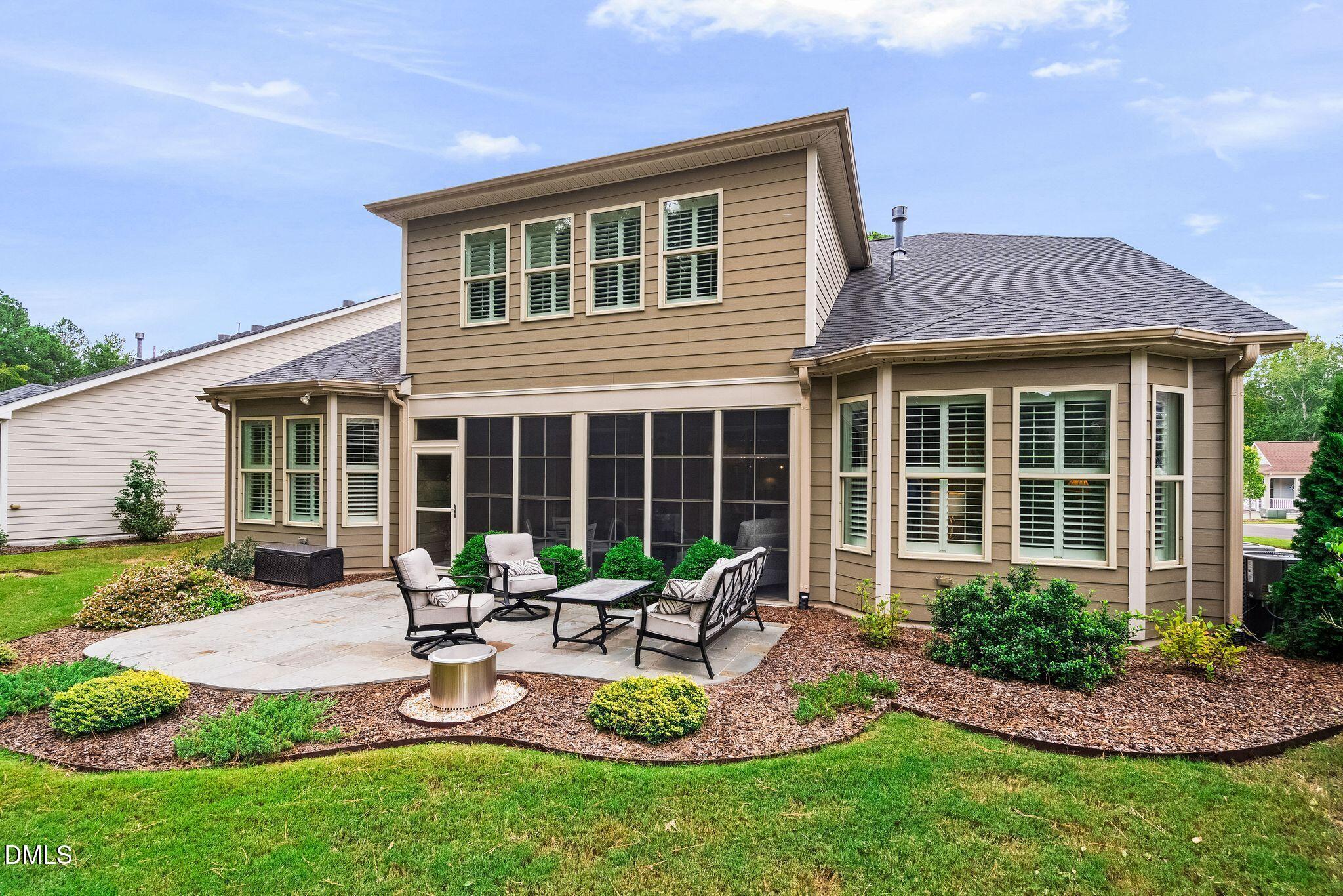 Rear of a tan two-story home with a screened porch and furnished stone patio.