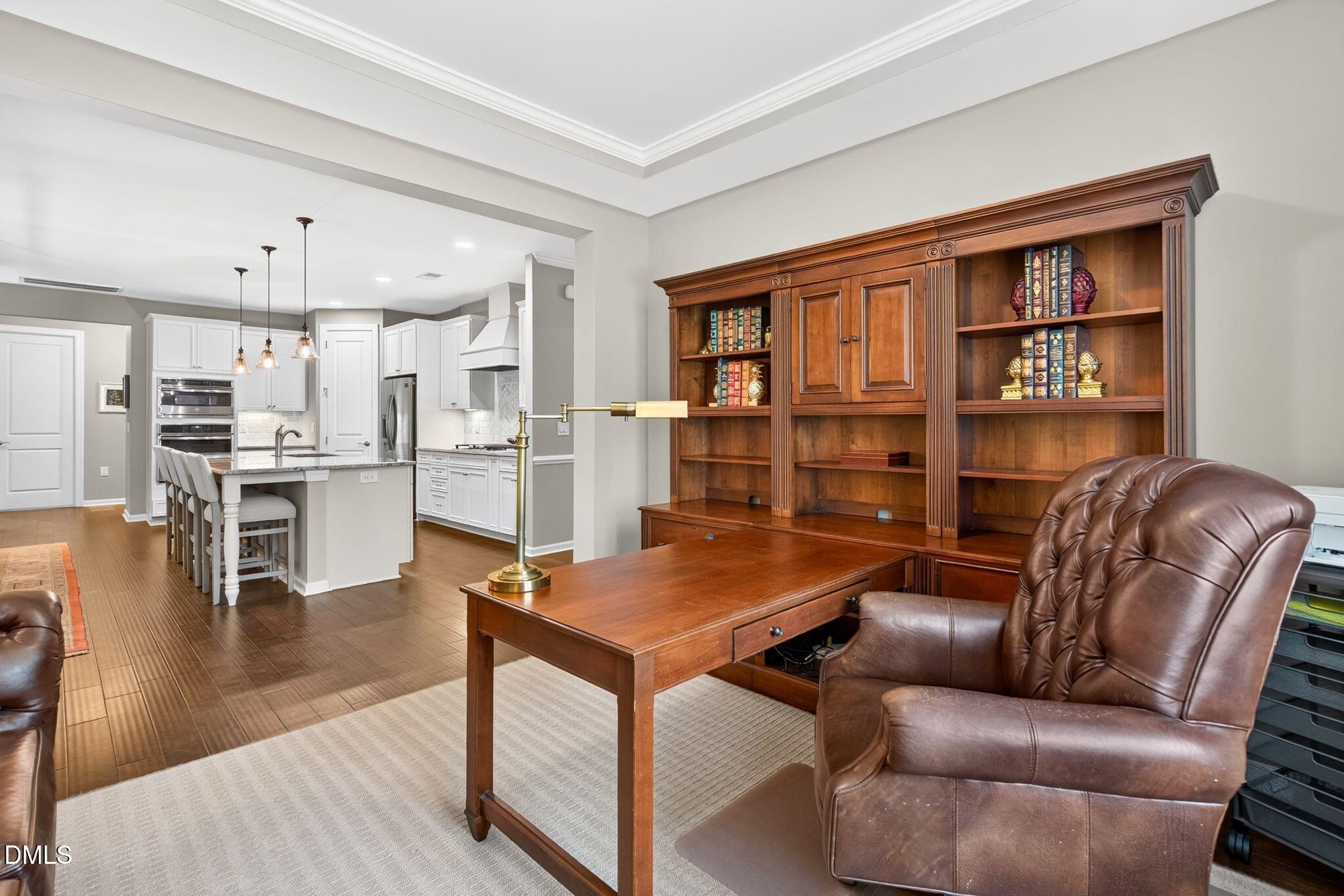 Home office with a built-in bookcase and leather armchair, opening onto a bright kitchen.