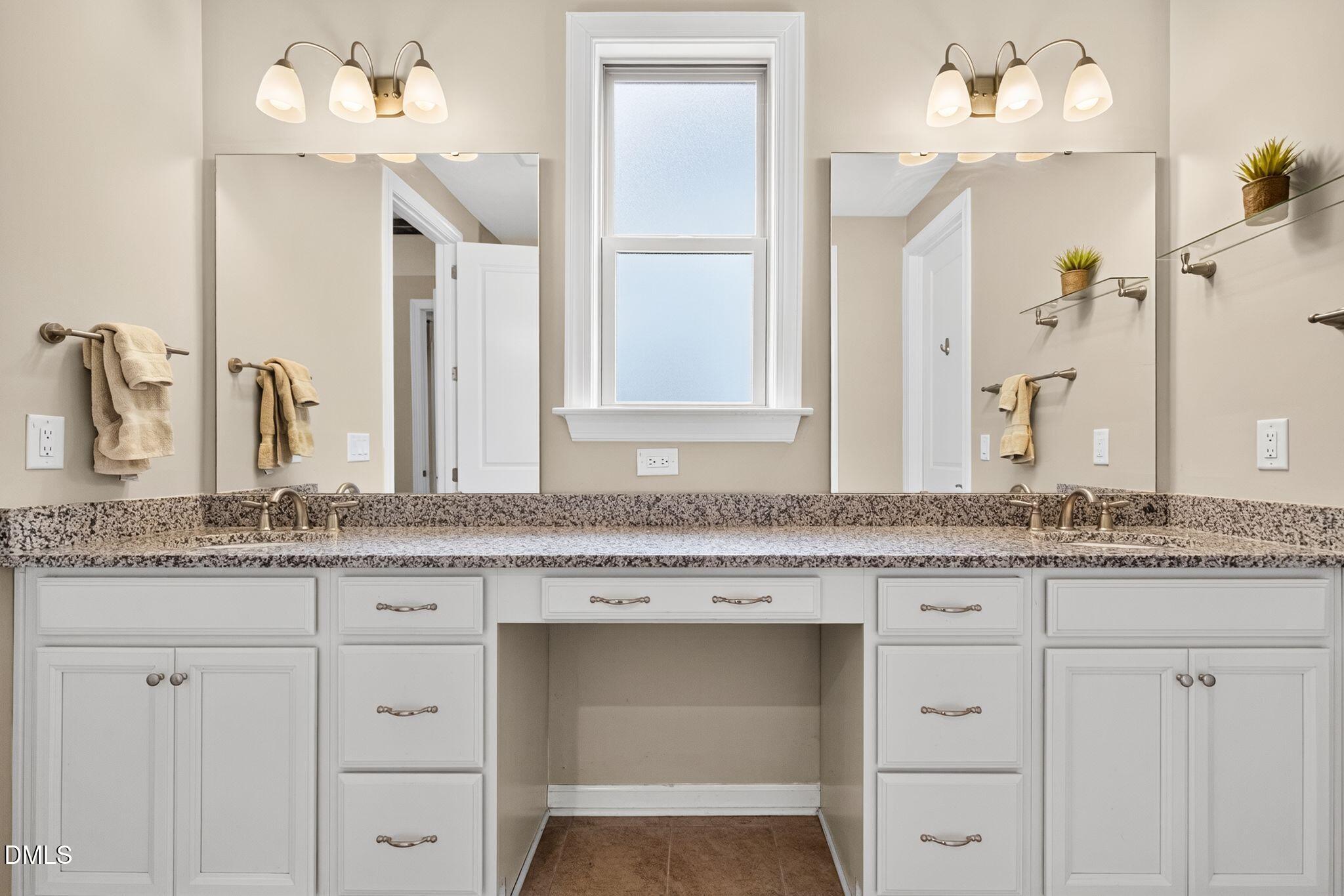 Bathroom vanity with granite counter, white cabinetry, double mirrors, and a tall frosted window.