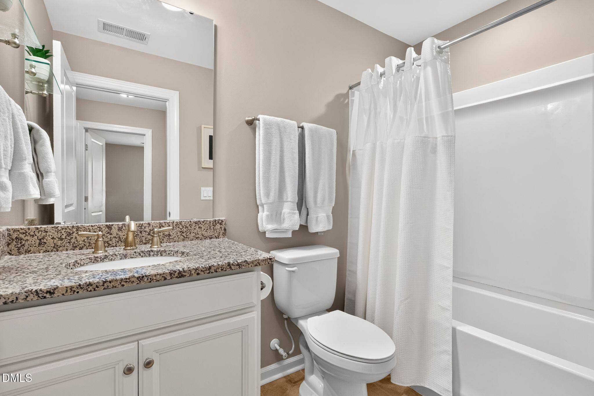 Bathroom with speckled granite vanity, brass-colored fixtures, toilet, and curtained bathtub.