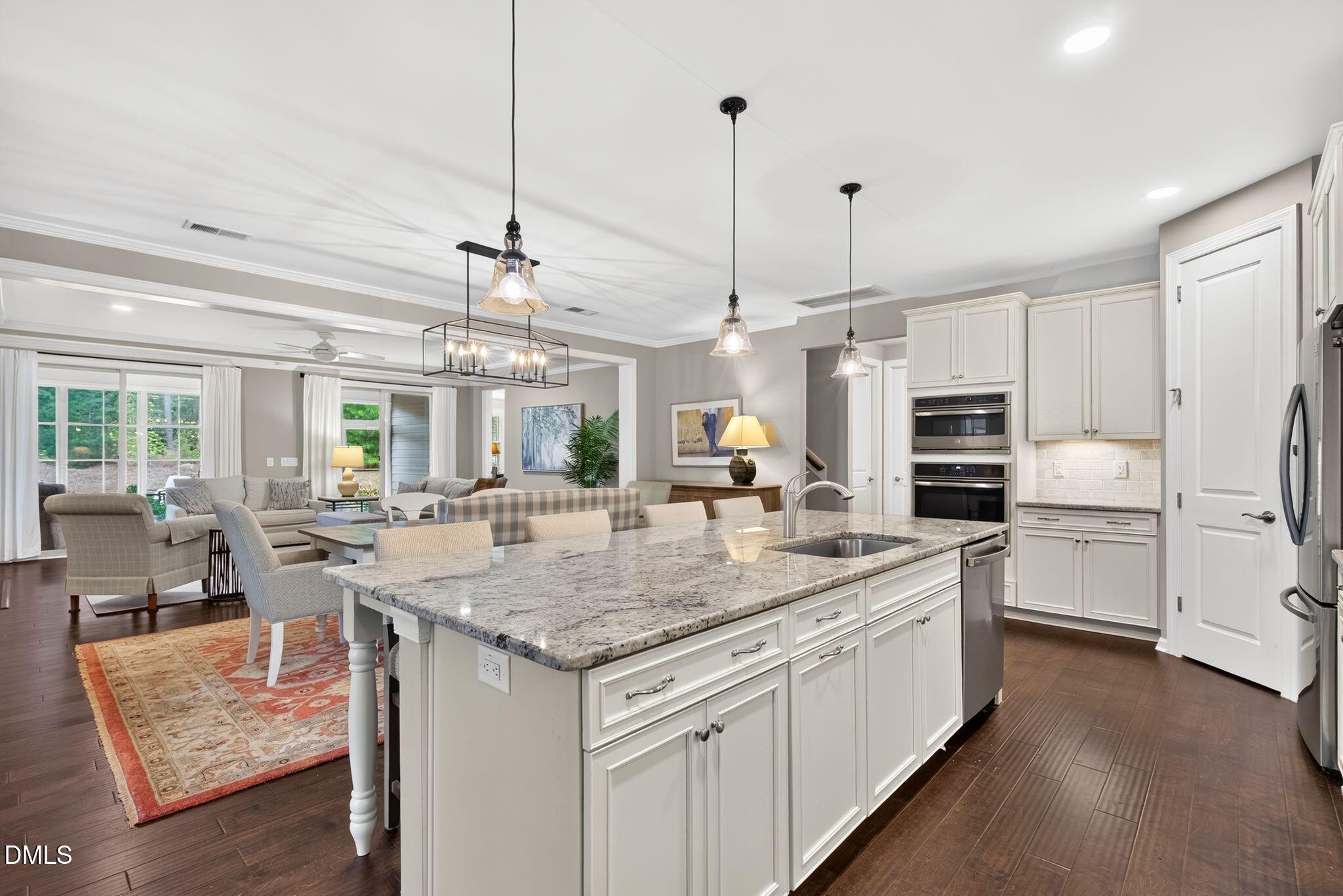Open-plan kitchen with a large granite island, white cabinets, pendant lights, and an adjoining living area.