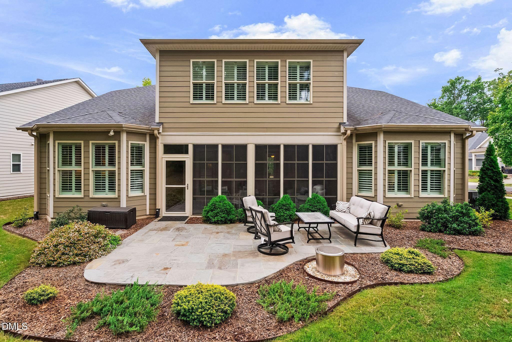 Home’s rear exterior with a screened porch and furnished stone patio.