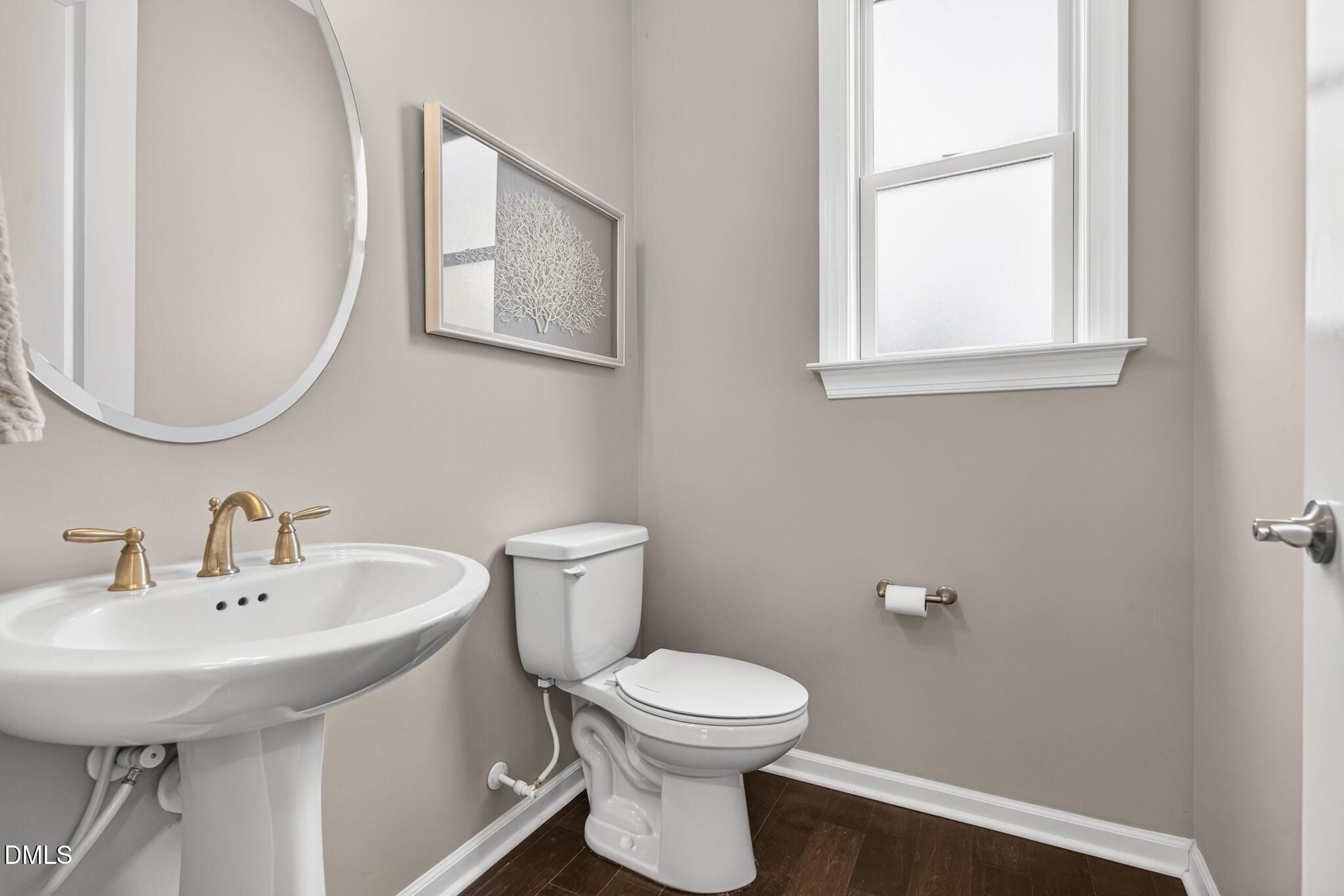 Half-bathroom with a pedestal sink, toilet, brass-tone fixtures, and a tall window.