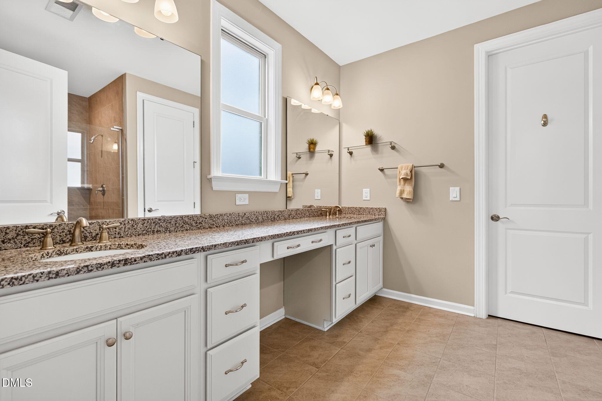 Bathroom with a long double vanity, speckled granite counters, and a tiled shower.