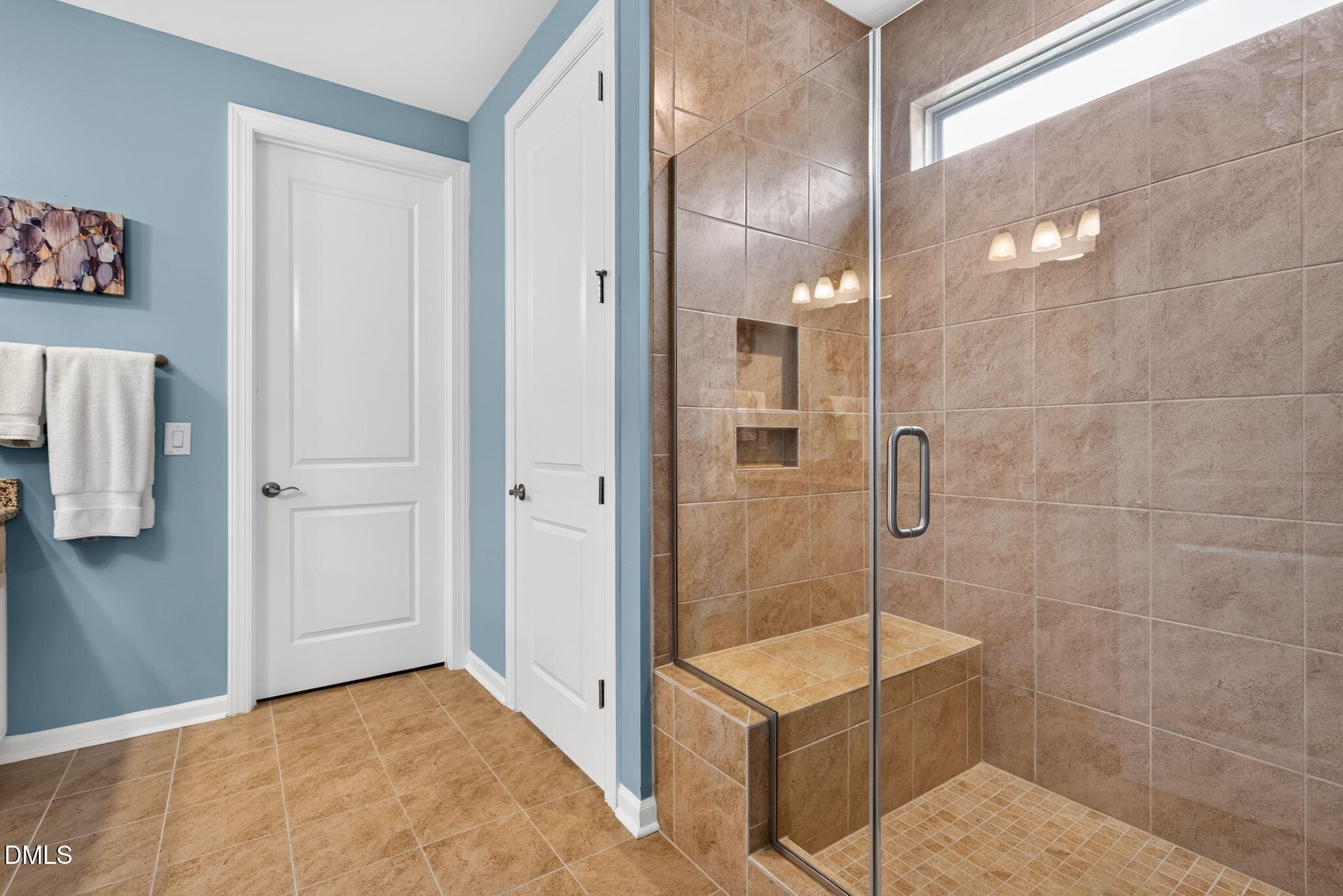 Bathroom with a glass-enclosed tiled walk-in shower, recessed niches, and a high window.