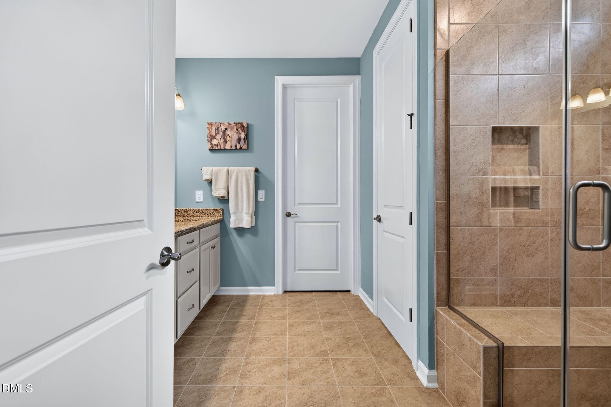 Bathroom with blue walls, granite vanity, tan tile floor, and glass-enclosed shower with a built-in niche.