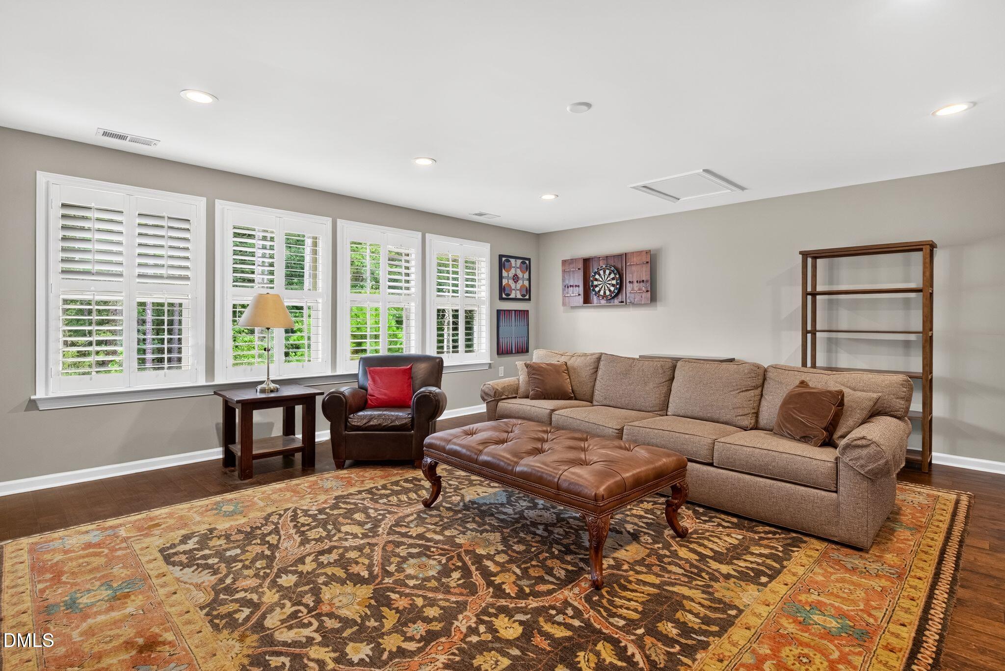 Living room with a beige sectional, leather ottoman, patterned rug, and shuttered windows.