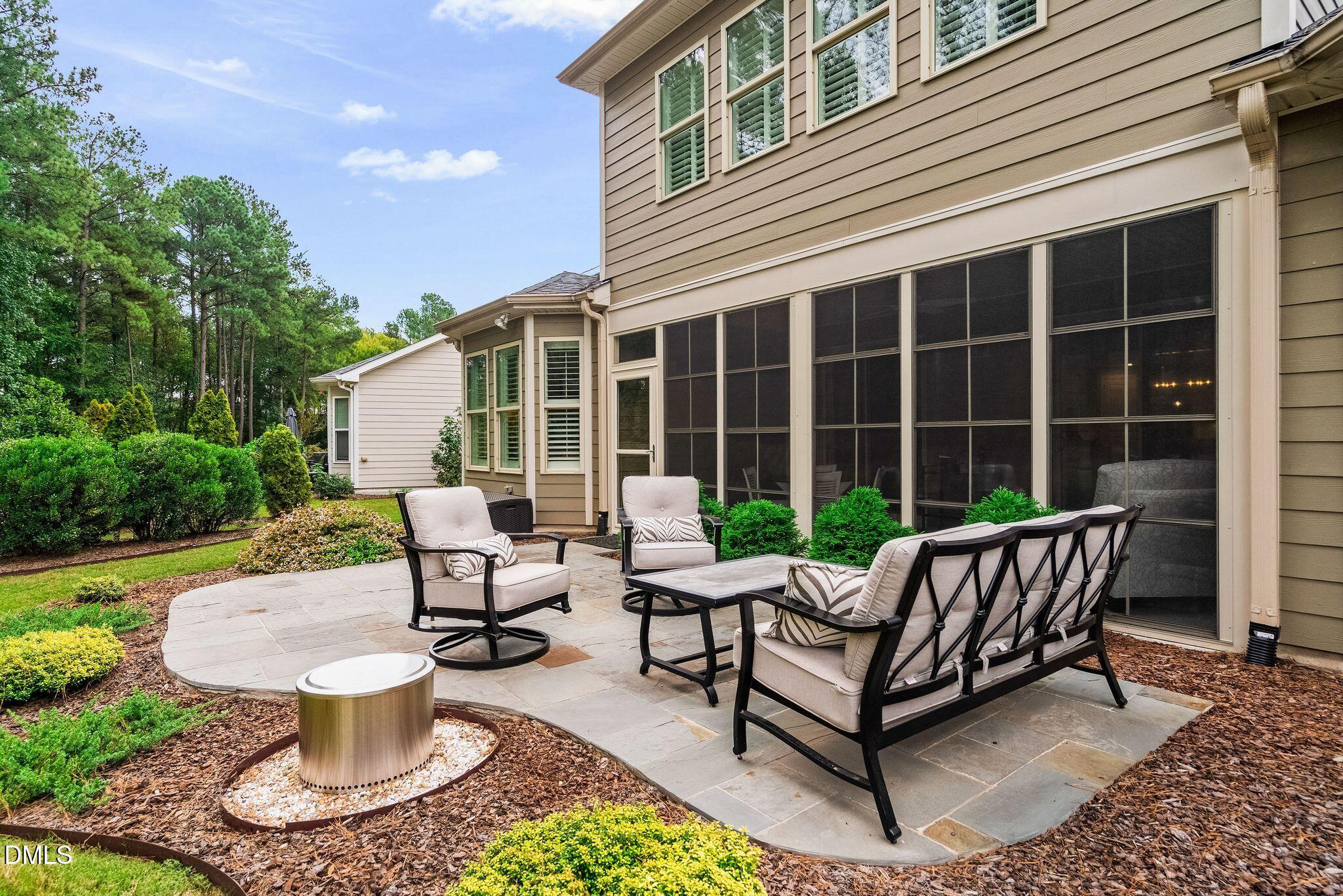 Stone backyard patio with cushioned seating beside the home's screened porch.