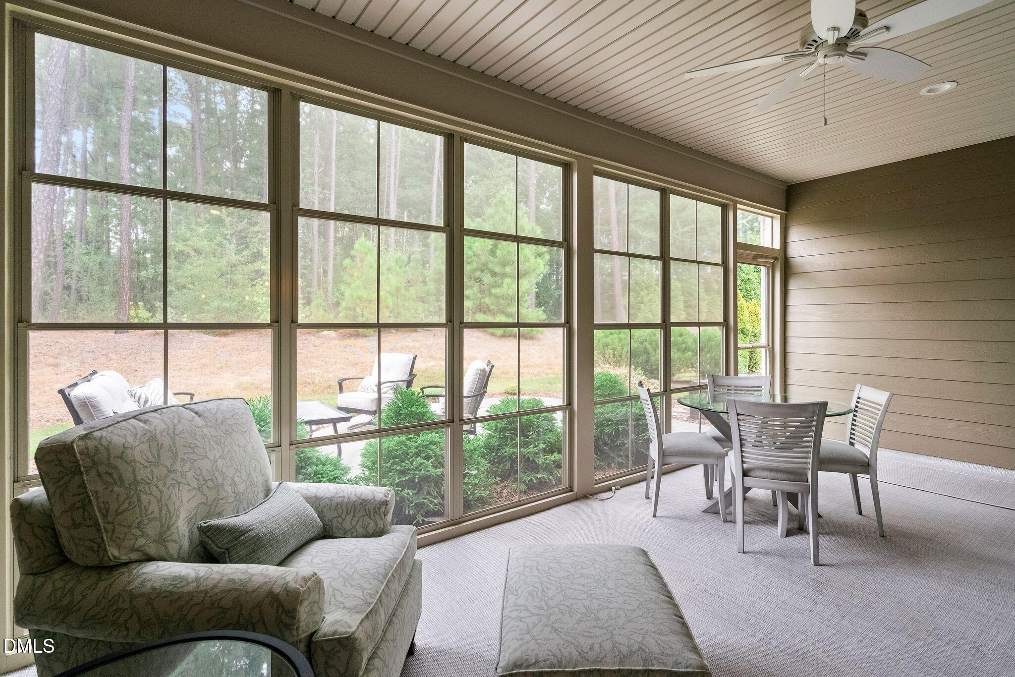 Furnished sunroom with tall windows overlooking trees and a dining table.