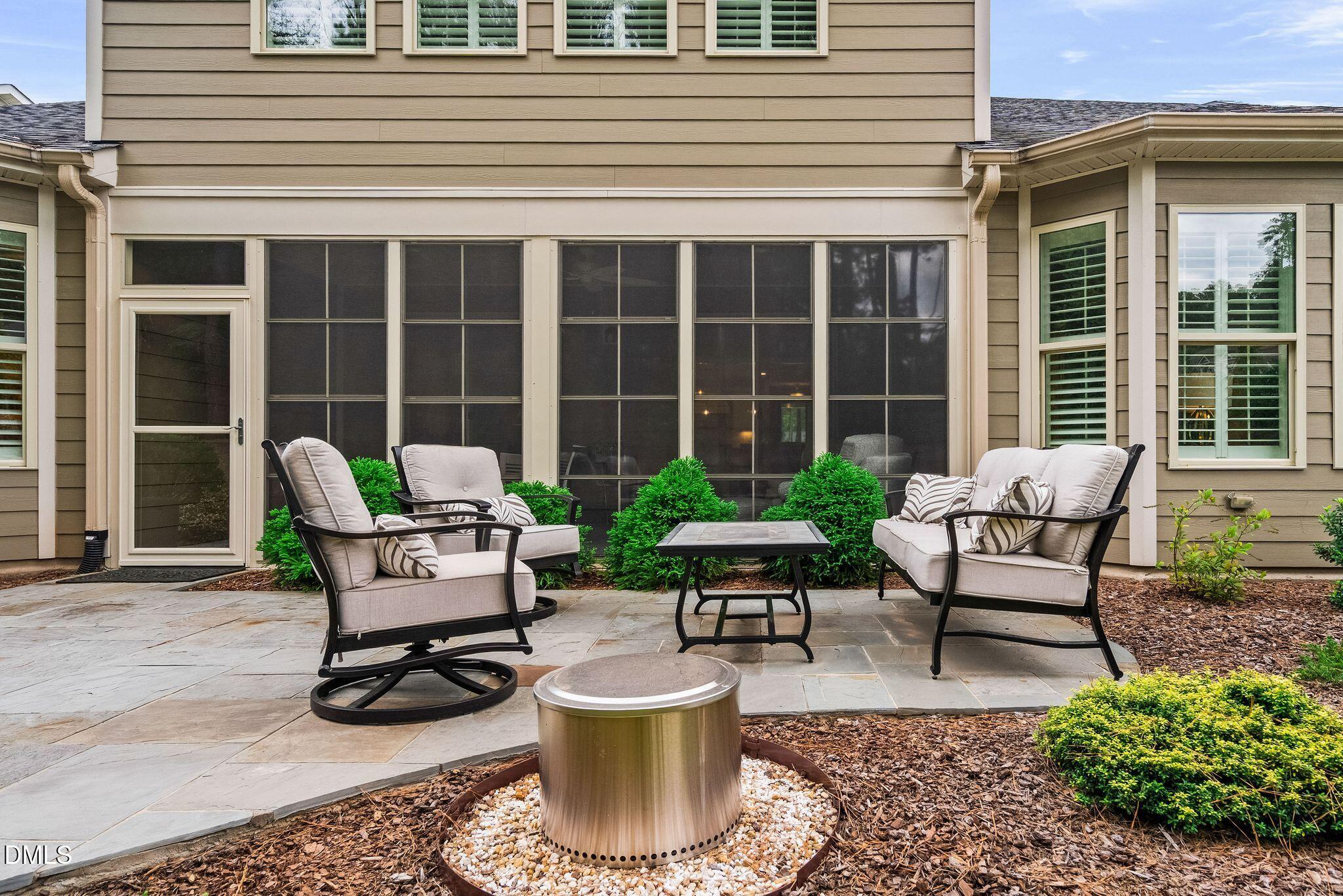 Stone patio with cushioned seating, a circular fire feature, and screened porch.