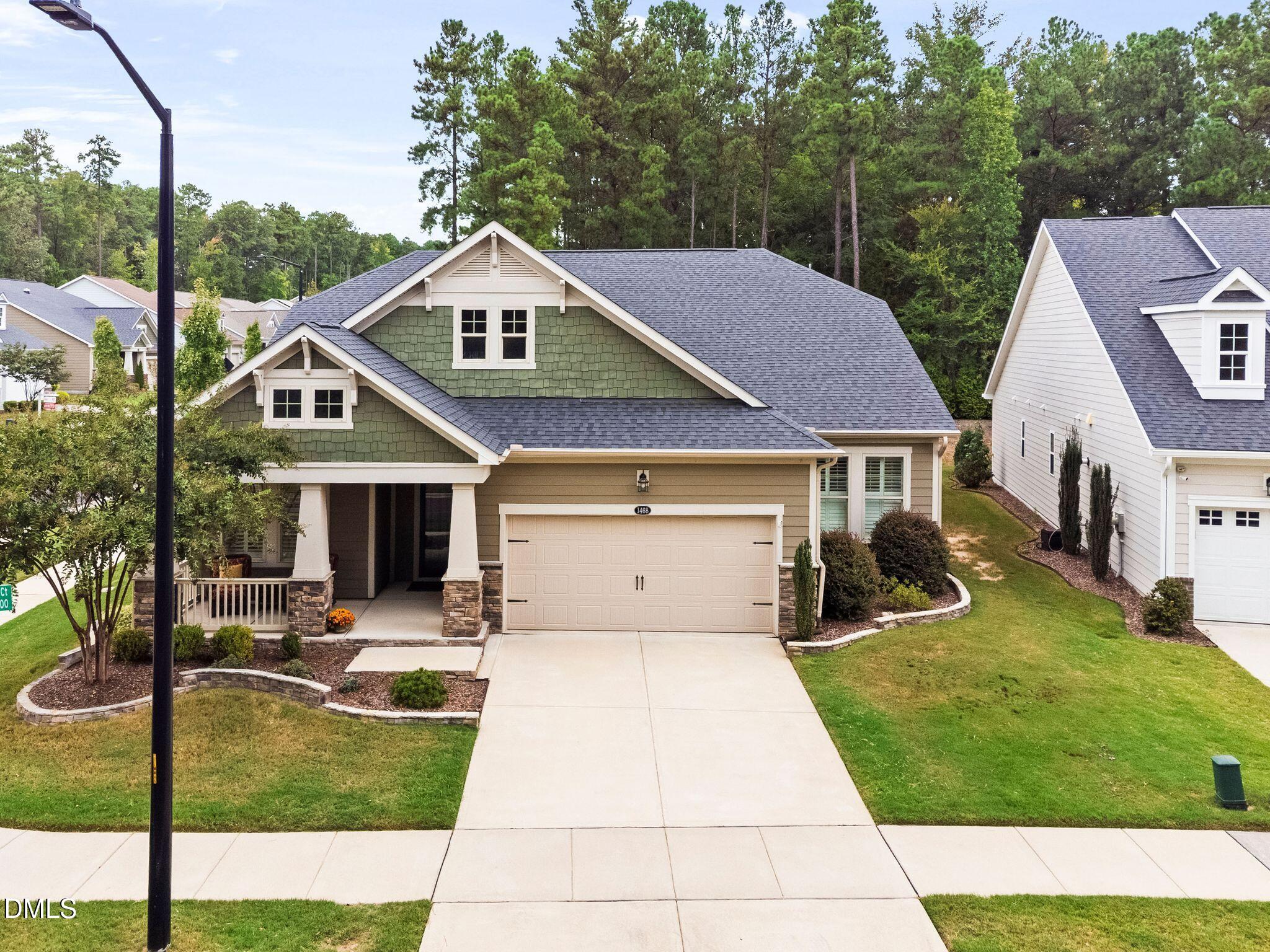 Green and tan two-story house with a covered porch, double garage, and wide concrete driveway.