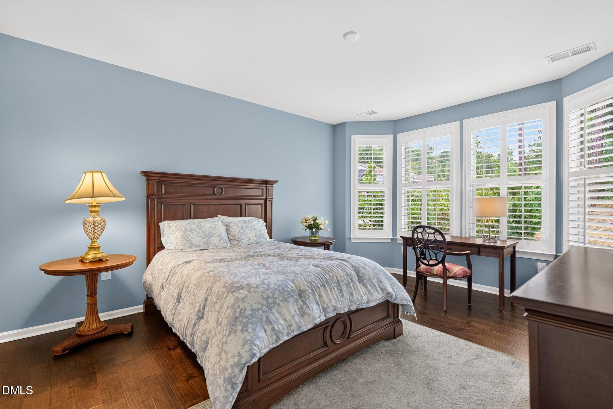 Bedroom with a dark wood bed, blue walls, and a desk beside shuttered windows.