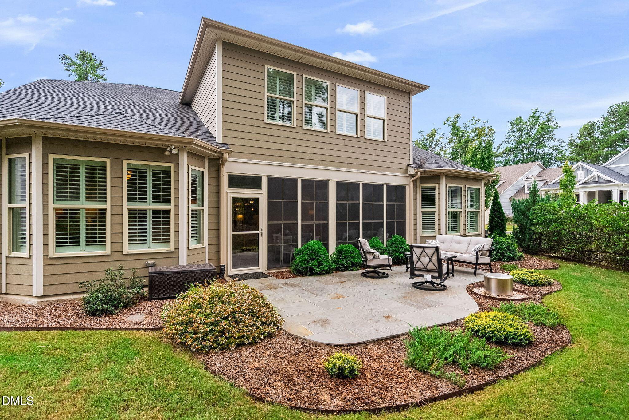 Home’s rear patio with a screened porch, stone terrace, outdoor seating, and landscaped yard.