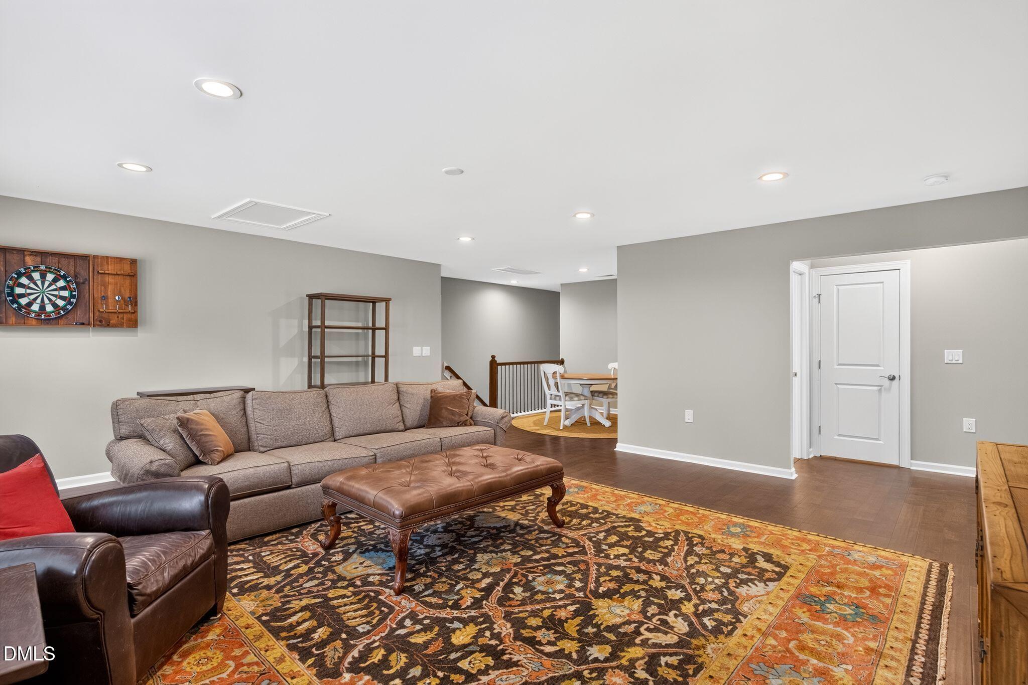 Furnished basement living room with a large patterned rug, sectional sofa, and wall-mounted dartboard.