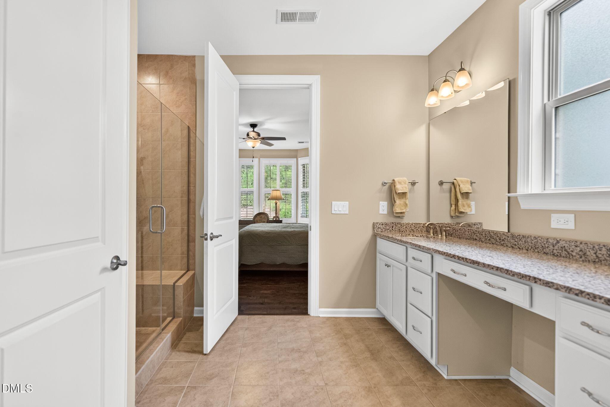 Bathroom with a glass-enclosed tile shower, granite vanity, and doorway to a bedroom.
