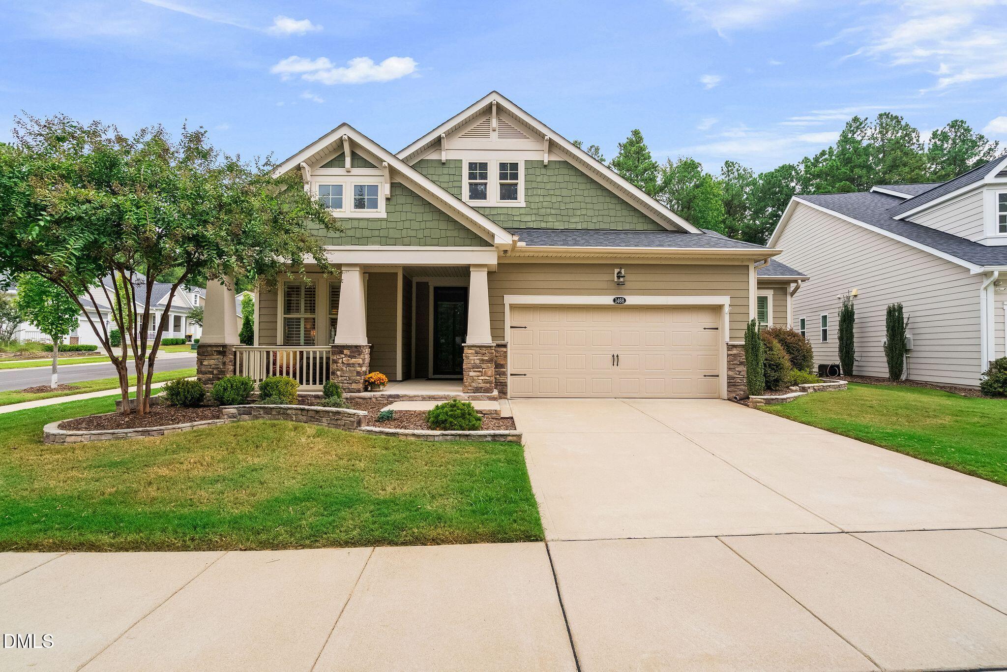 Suburban home with sage-green gables, a covered porch, stone accents, and an attached two-car garage.