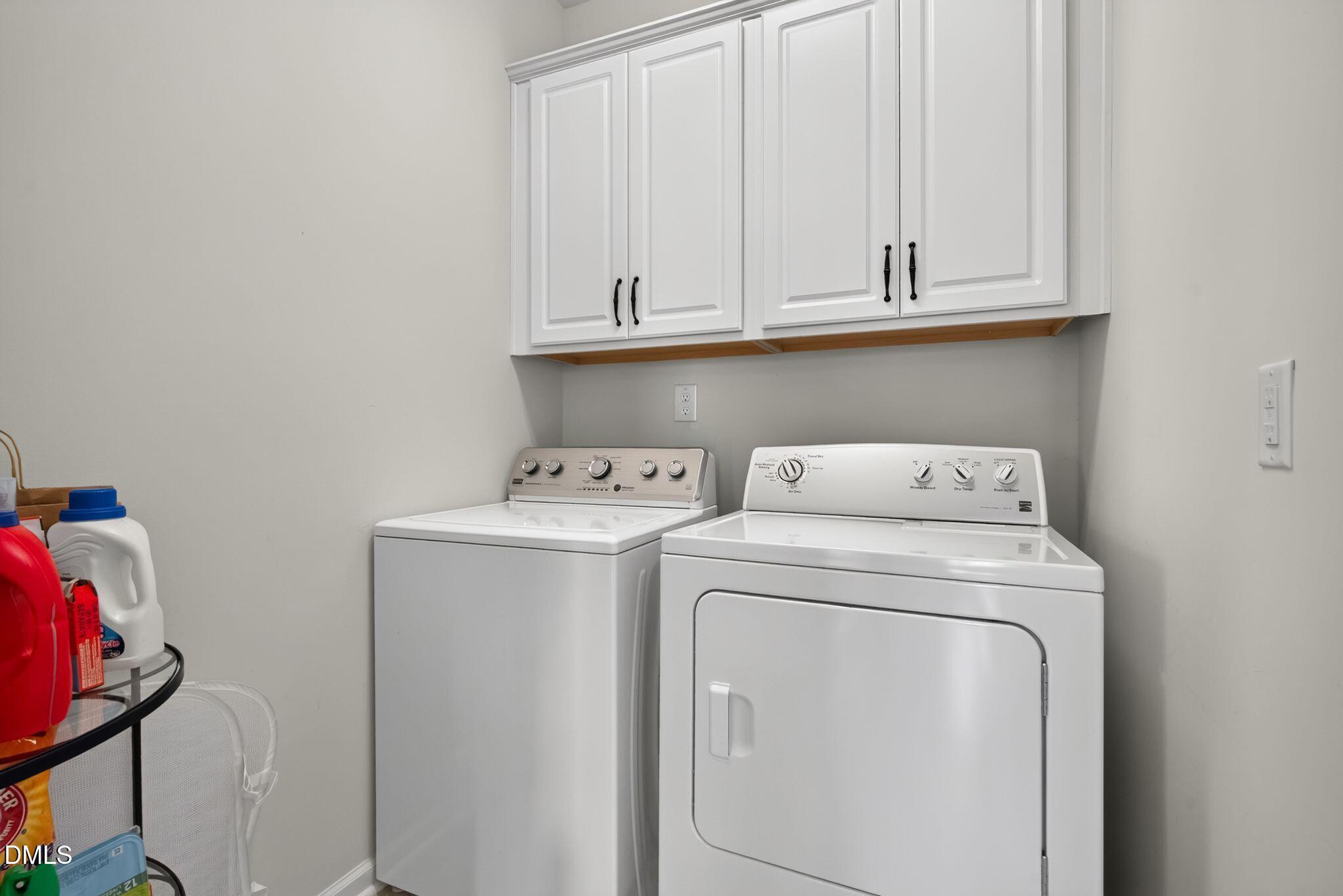 Laundry room with white washer and dryer beneath upper cabinets.