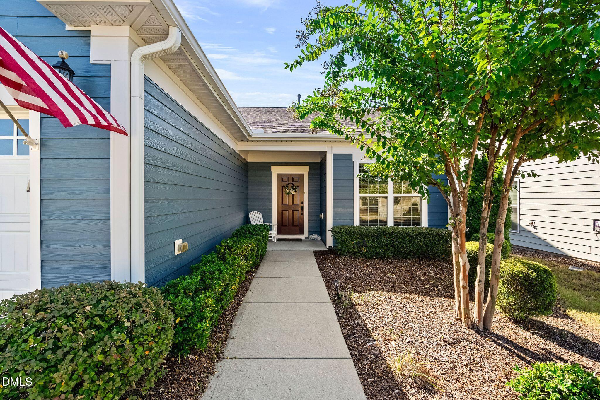 Blue-sided home entrance with an American flag, landscaped walkway, and mature tree.