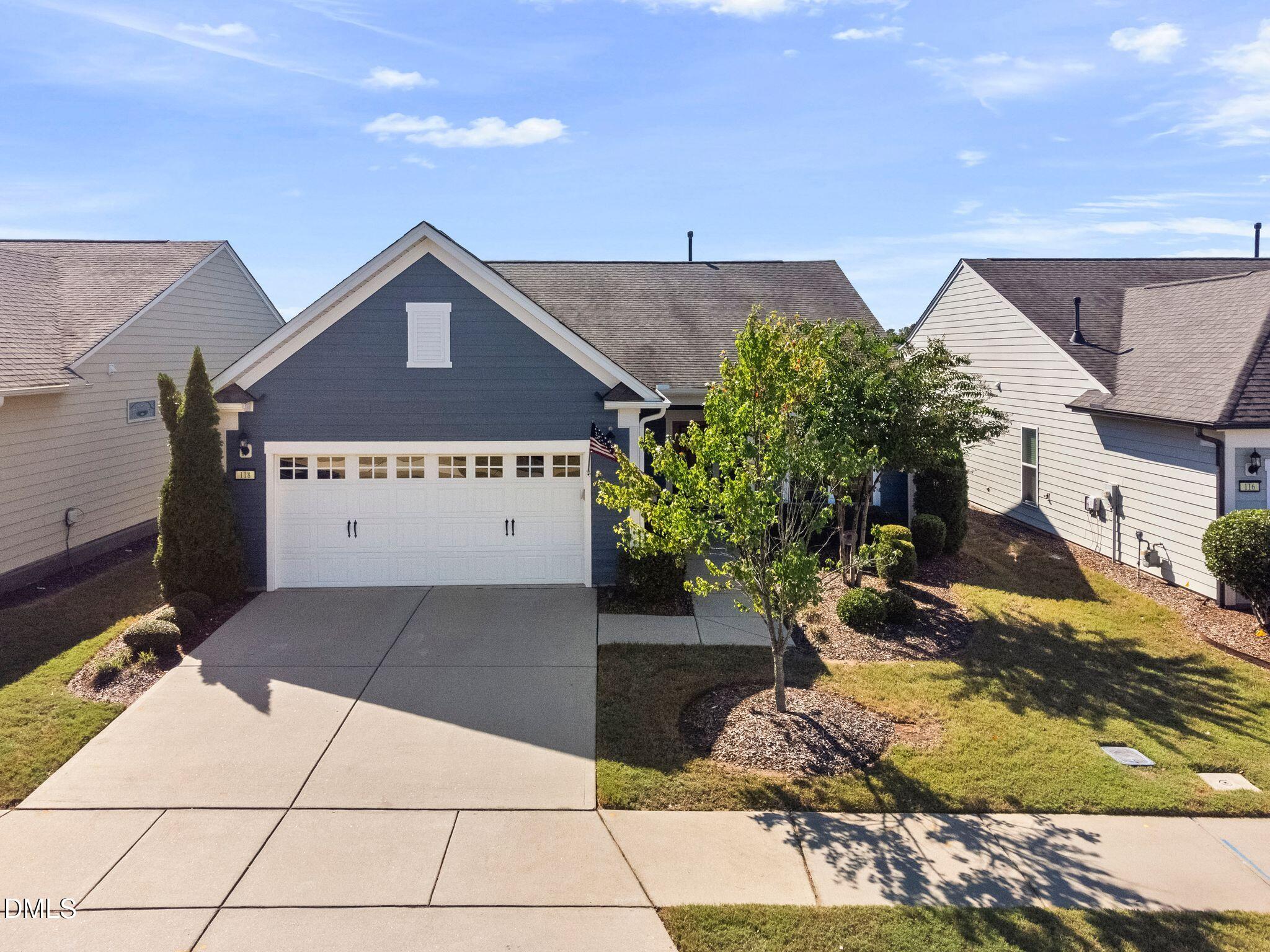 Blue house with white double garage, concrete driveway, and landscaped front yard.