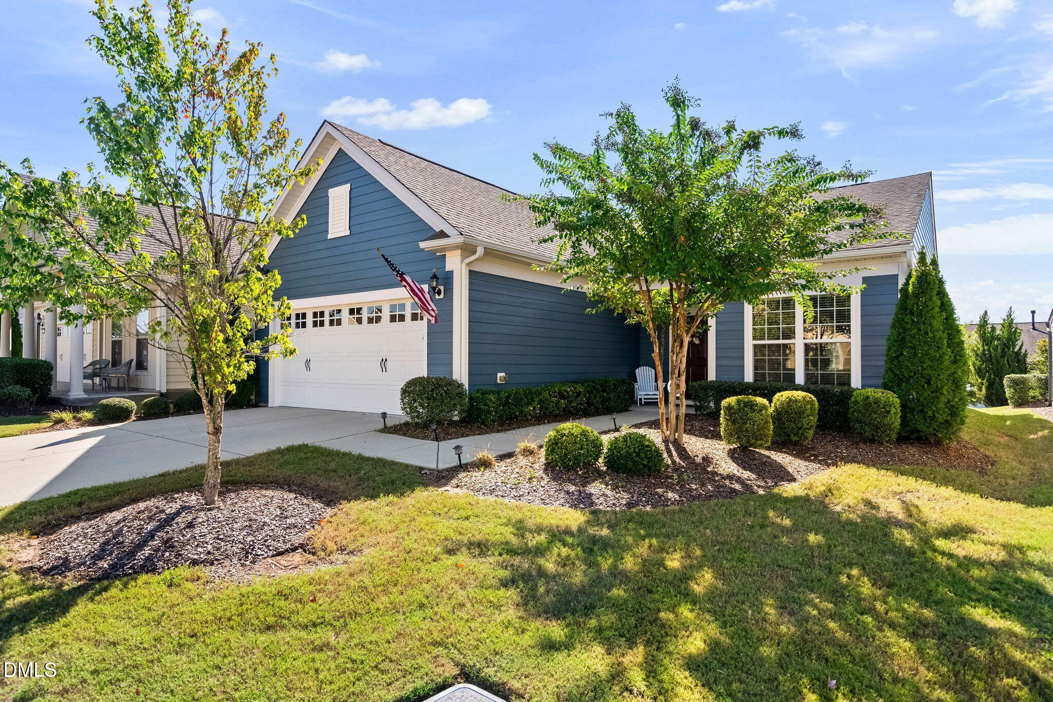 Blue-sided house with white trim, two-car garage, landscaped yard, and an American flag.