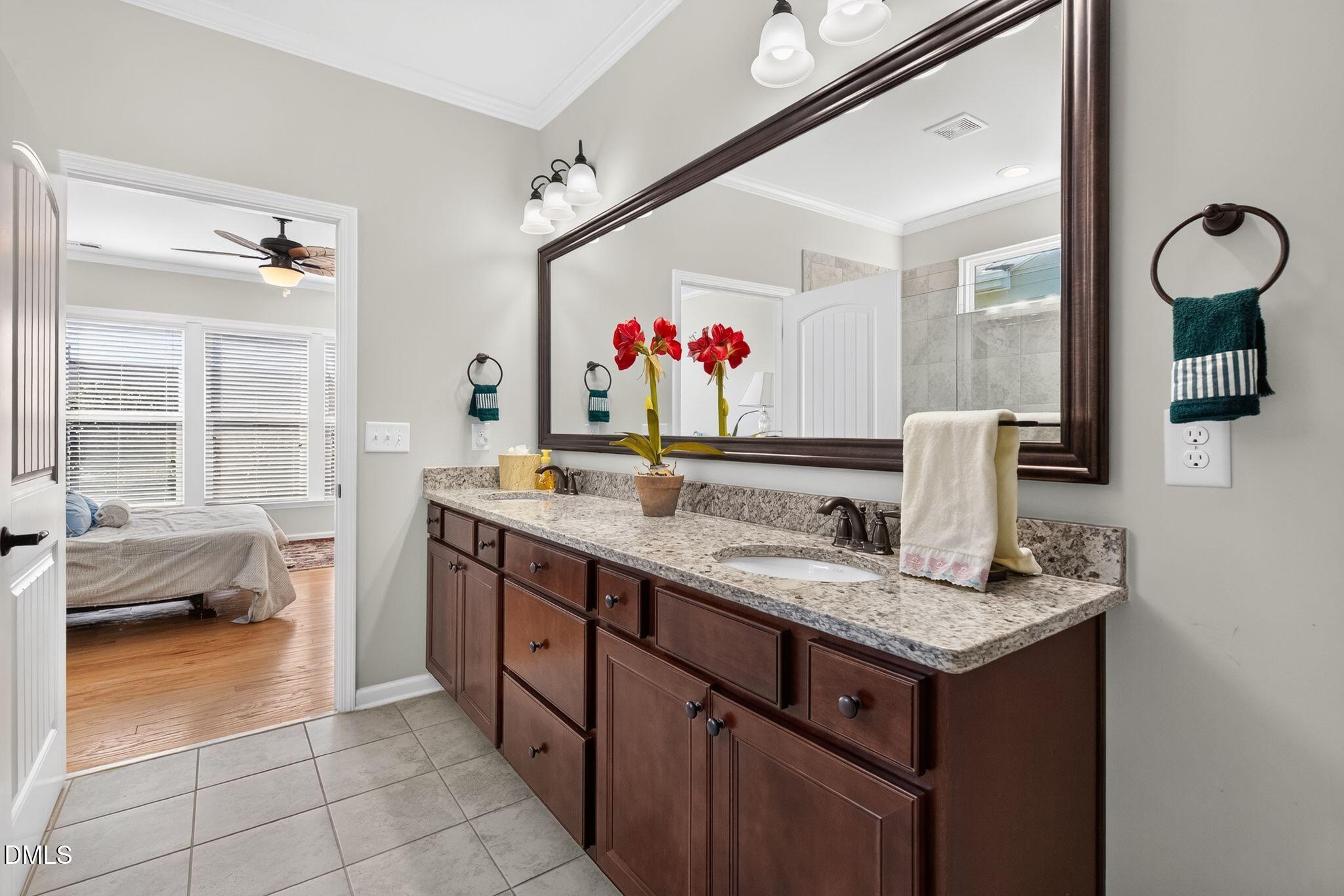 Bathroom vanity with dark wood cabinets, granite countertop, and a large mirror beside an open bedroom doorway.