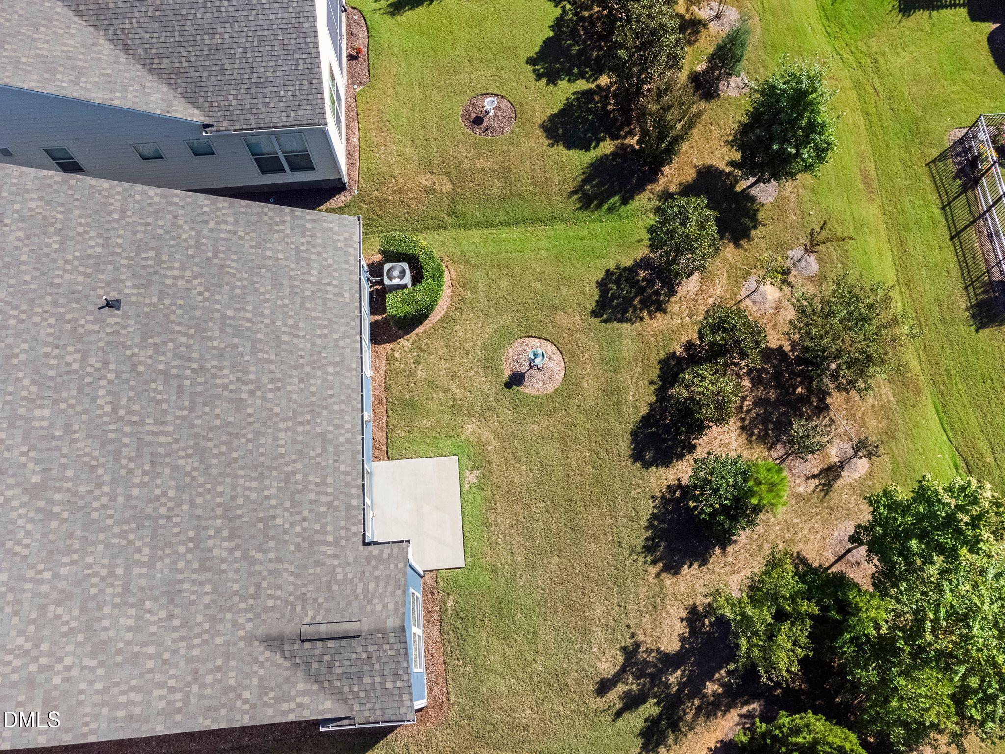 Aerial view of a home’s gray roof and grassy backyard with trees and a concrete patio.