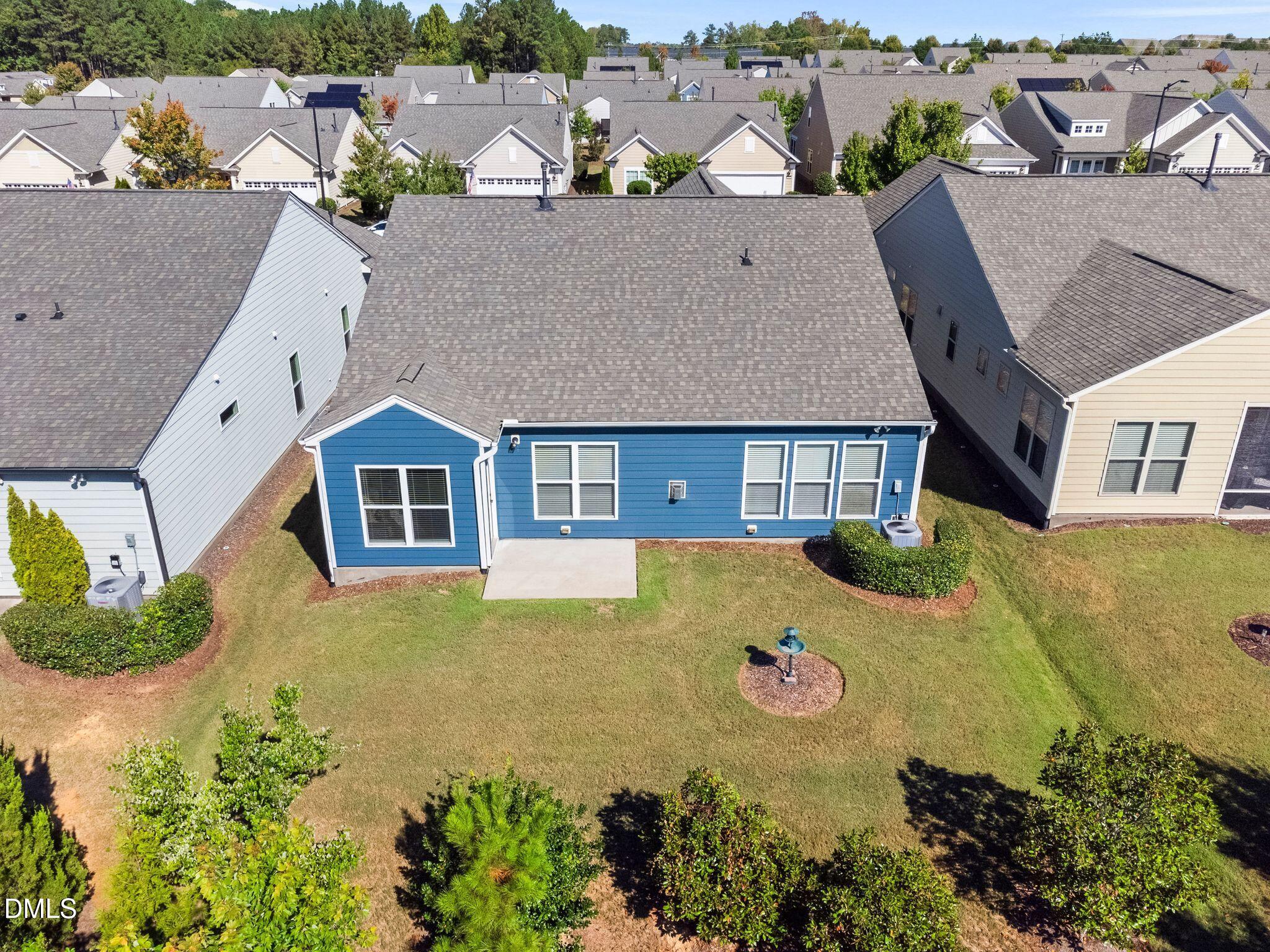 Aerial view of a blue house’s rear, backyard lawn, concrete patio, and surrounding homes.