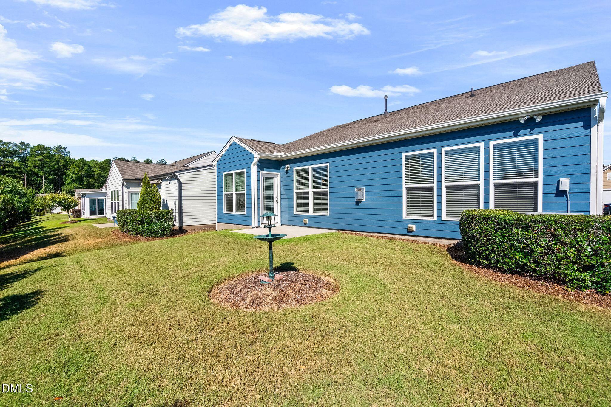 Blue-sided home’s rear exterior with white-trimmed windows, a broad lawn, and a bird feeder.