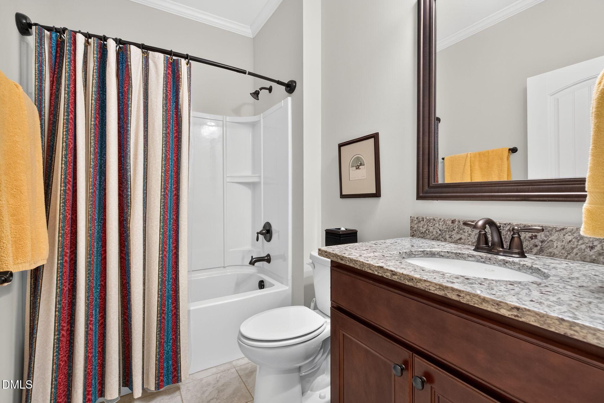 Bathroom with a striped shower curtain, white tub and toilet, and dark wood vanity with granite countertop.