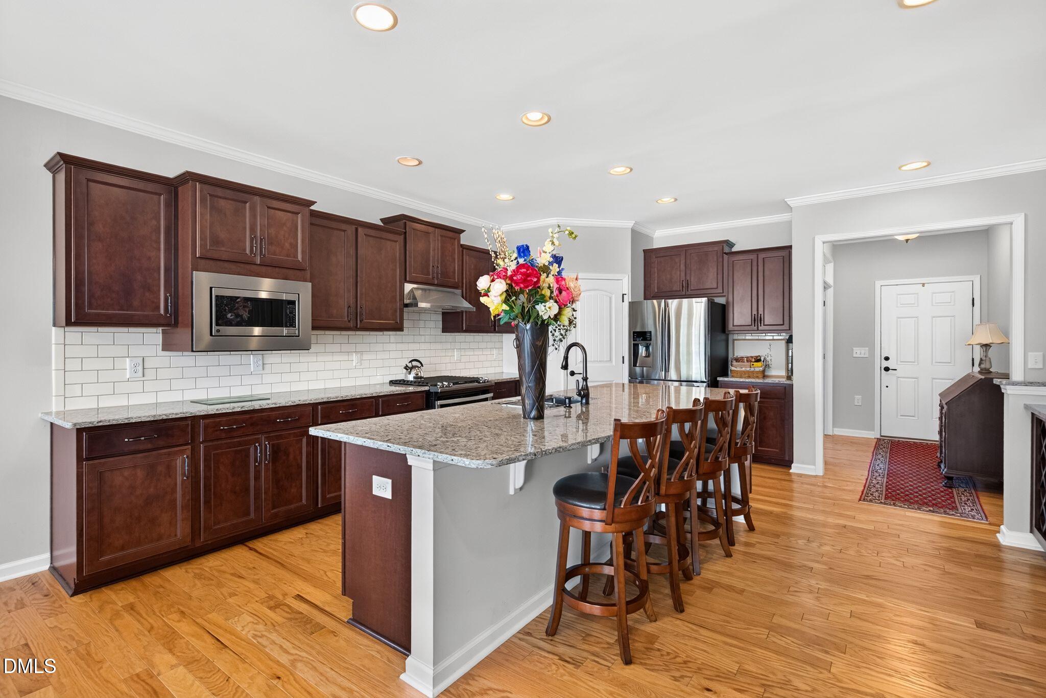 Kitchen with dark wood cabinetry, stainless steel appliances, granite island, and hardwood floors.