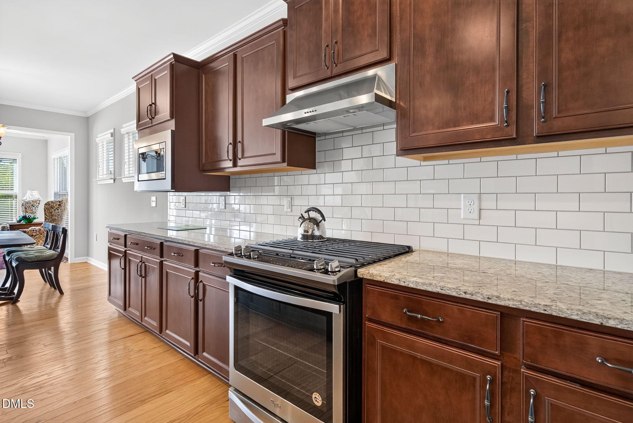 Kitchen with dark wood cabinetry, granite counters, white subway tile, and a stainless-steel gas range.