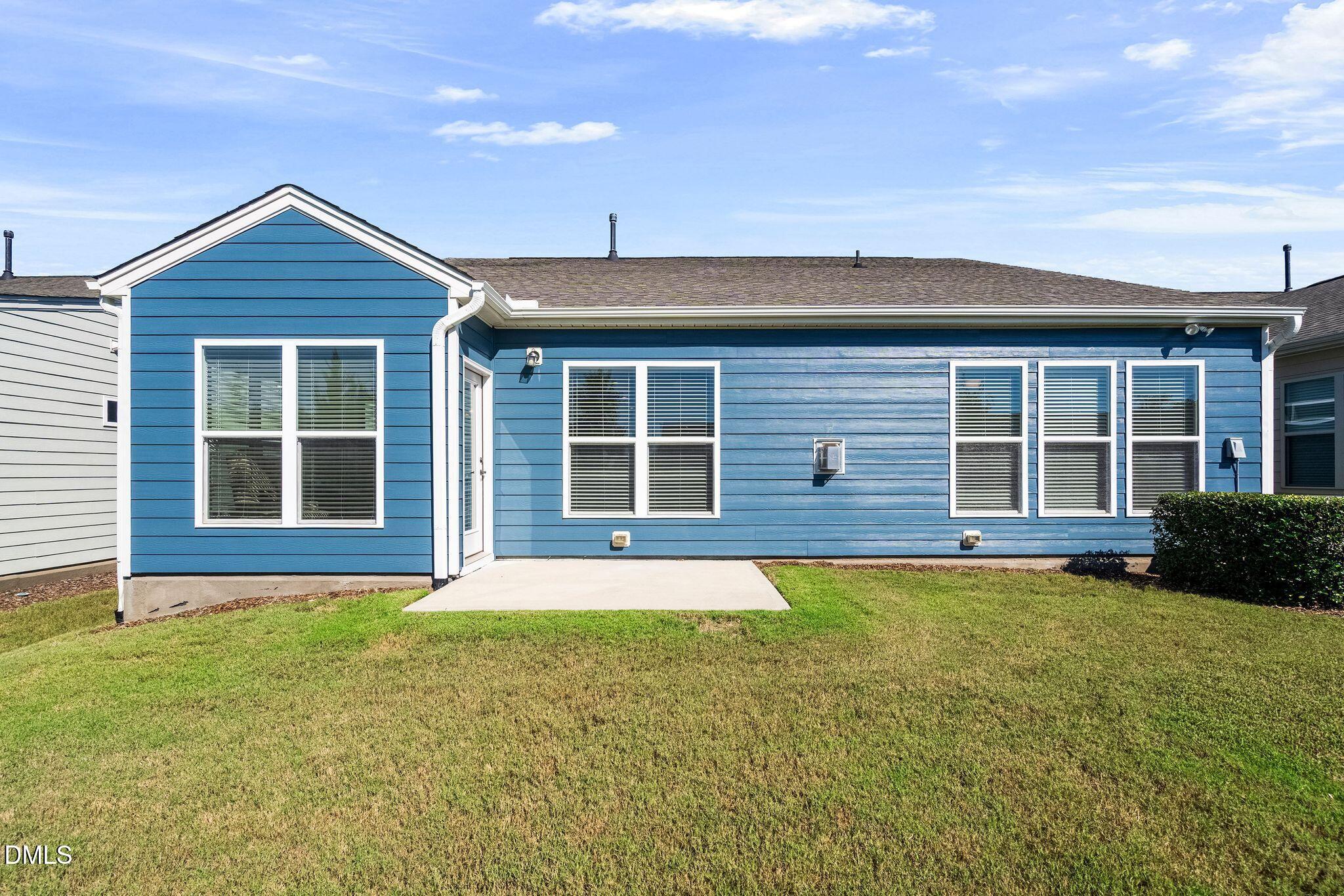 Blue house rear with white-trimmed windows, concrete patio, and broad lawn.